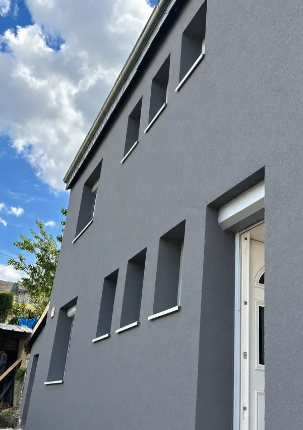 Façade grise après isolation extérieure, encadrements de fenêtres blancs et enduit uniforme