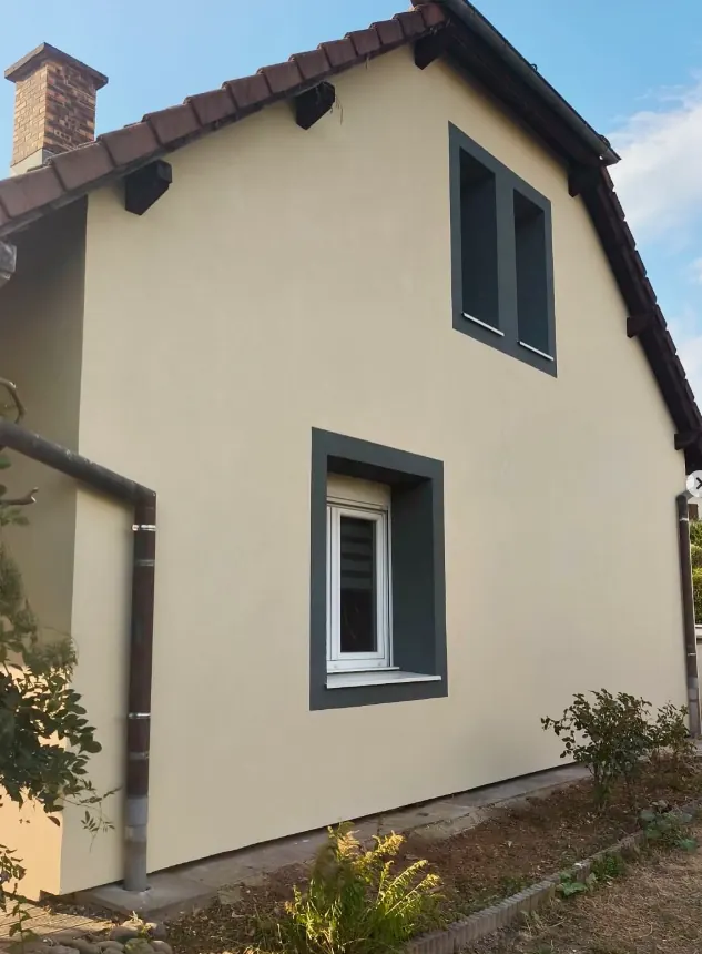 Pignon à l'enduit clair avec encadrements de fenêtres gris foncé après rénovation de façade